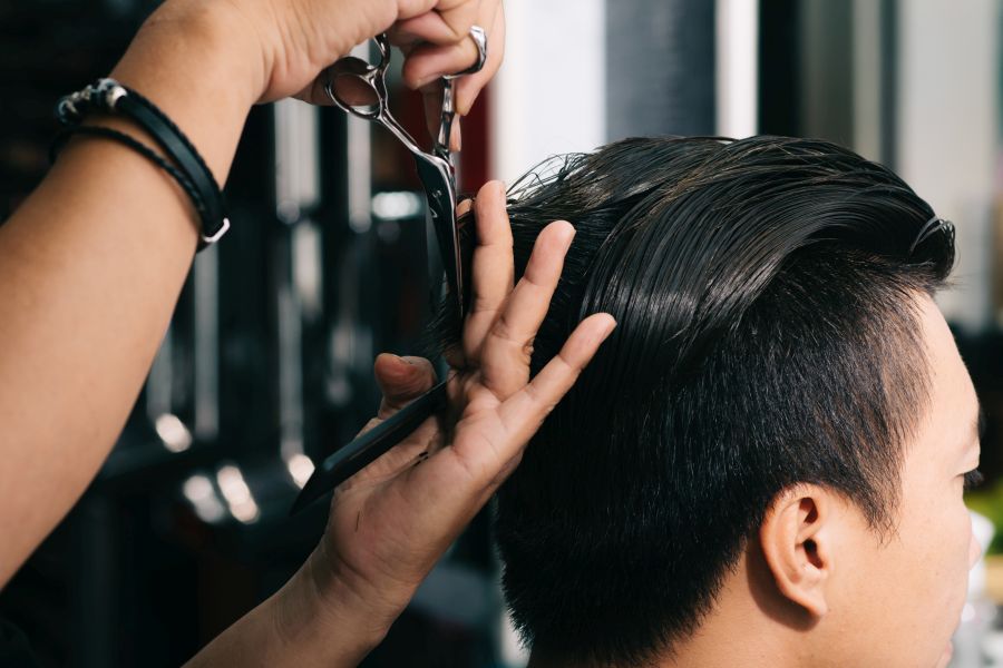 Nahaufnahme eines professionellen Friseurs, der einem jungen Mann mit einer Schere die Haare schneidet